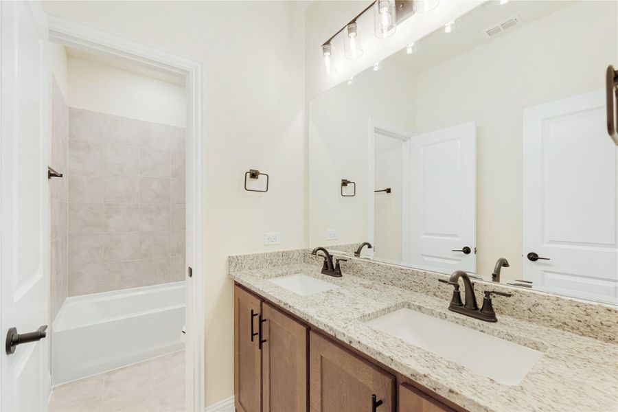 Bathroom with double sink vanity, granite countertop, wood cabinets, and tiled tub-shower combo Bathroom with double sink vanity, granite countertop, wood cabinets, and tiled tub-shower combo