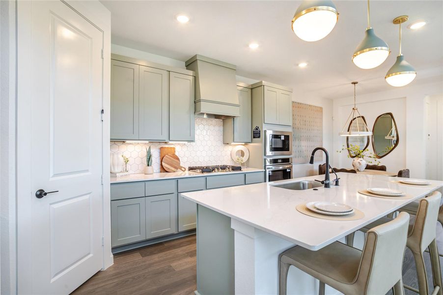 This modern kitchen features sleek sage green cabinetry, a spacious white quartz island with seating, and stylish pendant lighting. The backsplash has a hexagonal tile design, and stainless steel appliances add a contemporary touch. Perfect for entertaining and everyday living. This modern kitchen features sleek sage green cabinetry, a spacious white quartz island with seating, and stylish pendant lighting. The backsplash has a hexagonal tile design, and stainless steel appliances add a contemporary touch. Perfect for entertaining and everyday living.
