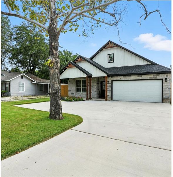 View of front facade with board and batten siding, a shingled roof, driveway, and stone siding