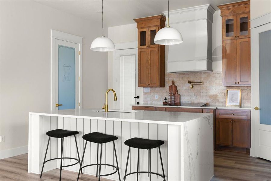 Kitchen featuring a center island with sink, pendant lighting, and custom range hood