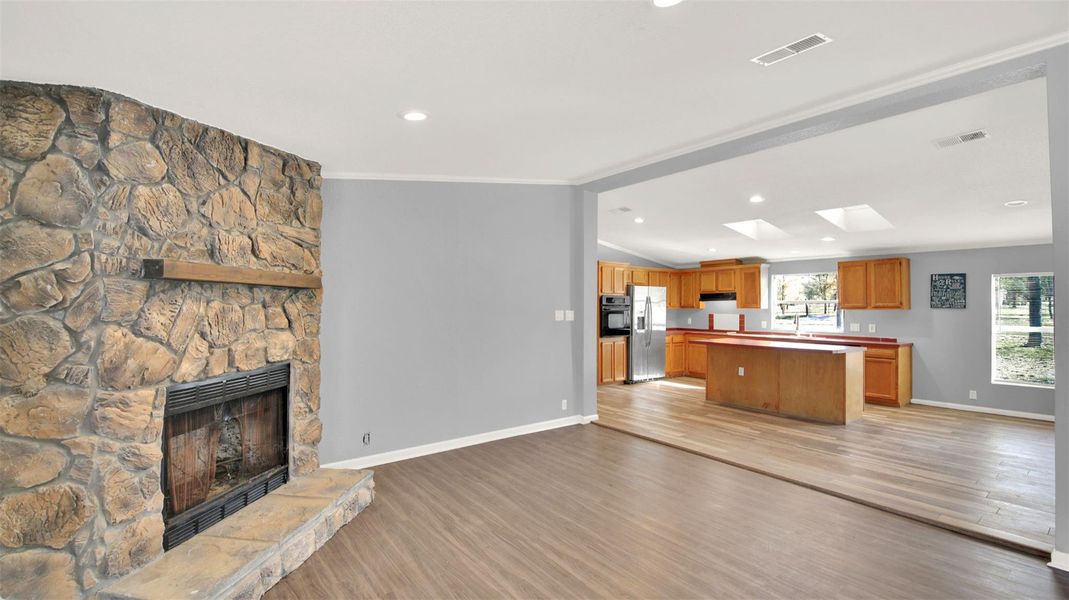 Unfurnished living room with a stone fireplace, light wood-style flooring, lofted ceiling, and crown molding