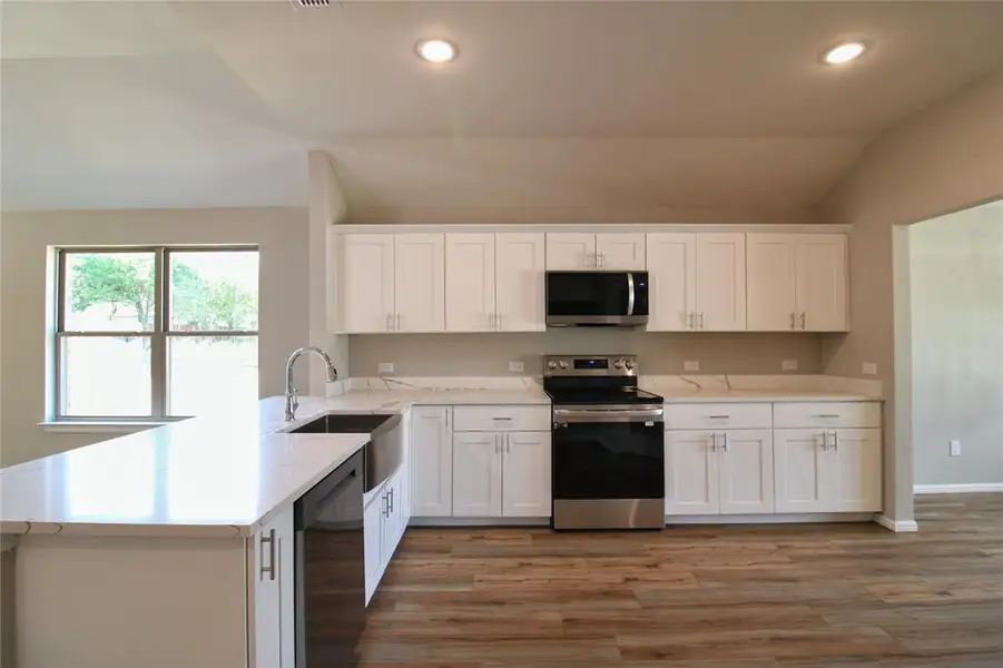 Kitchen featuring lofted ceiling, white cabinetry, stainless steel appliances, light wood finished floors, and a peninsula