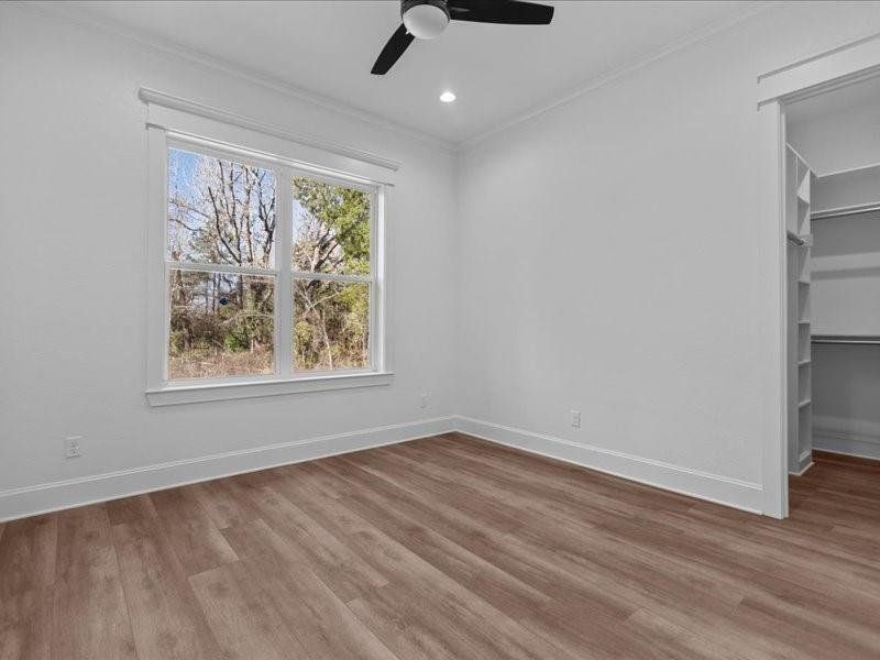 Unfurnished bedroom with a walk in closet, light wood-type flooring, ornamental molding, ceiling fan, and recessed lighting