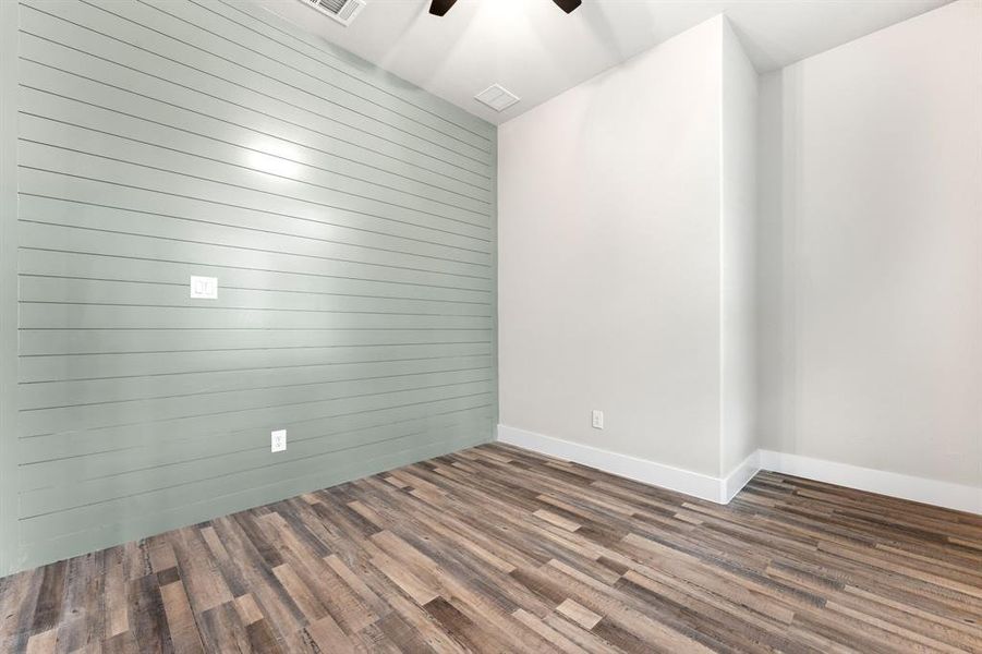 Empty room featuring wood walls, dark wood-type flooring, and ceiling fan