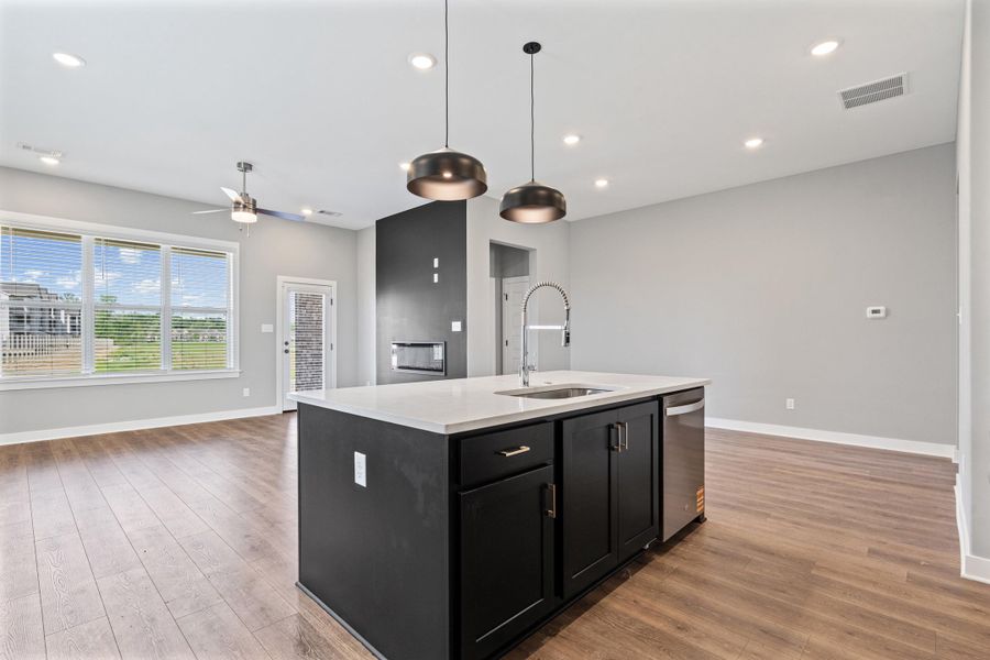 Kitchen with dark cabinetry, a center island with sink, open floor plan, pendant lighting, and a ceiling fan