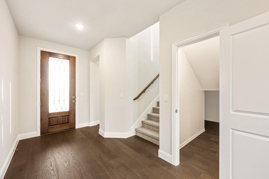 Entryway with dark hardwood floors, wood front door with glass panel, and carpeted staircase with wood railing Entryway with dark hardwood floors, wood front door with glass panel, and carpeted staircase with wood railing