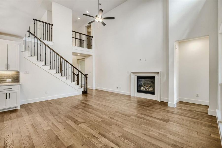 Unfurnished living room featuring a ceiling fan, a glass covered fireplace, light wood finished floors, a high ceiling, and recessed lighting
