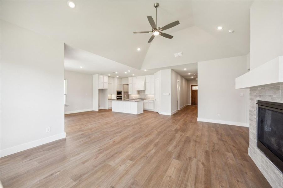 Unfurnished living room with ceiling fan, high vaulted ceiling, and light wood-type flooring