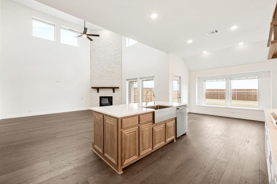 Open-concept kitchen with wood island, farmhouse sink, and stone fireplace in living area with vaulted ceiling and hardwood floors