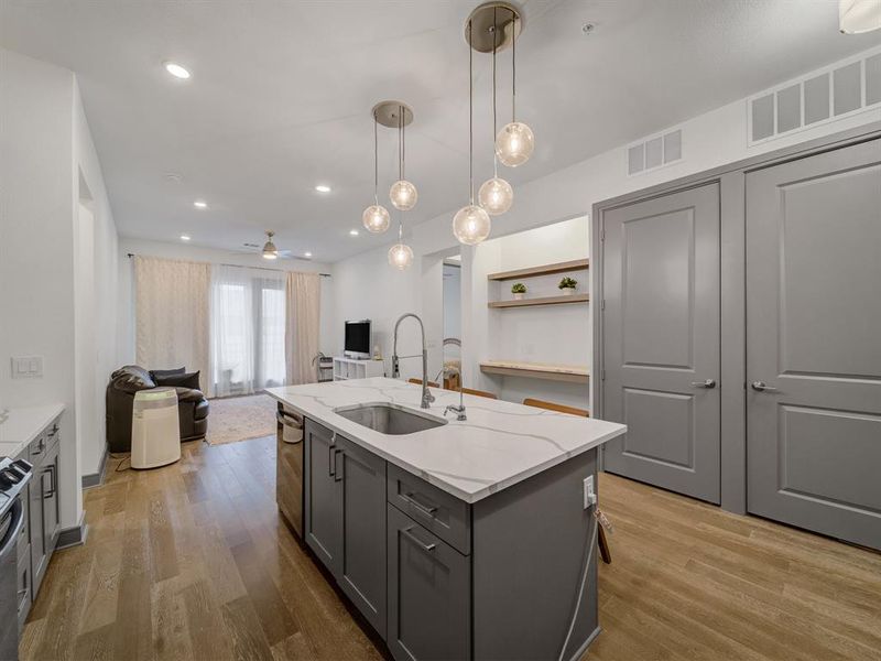 Kitchen featuring gray cabinets, open floor plan, pendant lighting, a center island with sink, and light wood-type flooring
