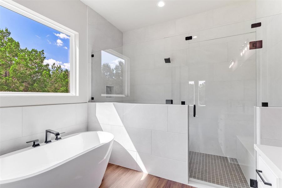 Full bath featuring pet washing area, a shower stall, a soaking tub, wood finished floors, and tile walls