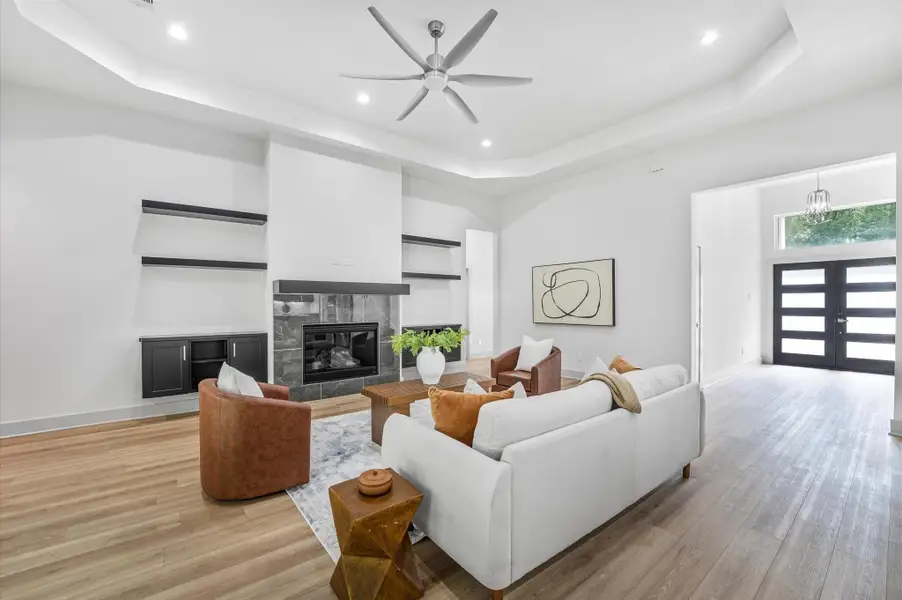 This modern living room features an open layout with high ceilings, a sleek ceiling fan, and recessed lighting. It includes a stylish fireplace with built-in shelving, light wood flooring, and large windows for natural light. The entryway has a contemporary door and a chic chandelier. This modern living room features an open layout with high ceilings, a sleek ceiling fan, and recessed lighting. It includes a stylish fireplace with built-in shelving, light wood flooring, and large windows for natural light. The entryway has a contemporary door and a chic chandelier.