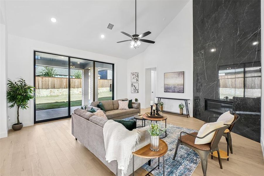 Living area with light wood-style floors, a high end fireplace, high vaulted ceiling, a ceiling fan, and recessed lighting Living area with light wood-style floors, a high end fireplace, high vaulted ceiling, a ceiling fan, and recessed lighting