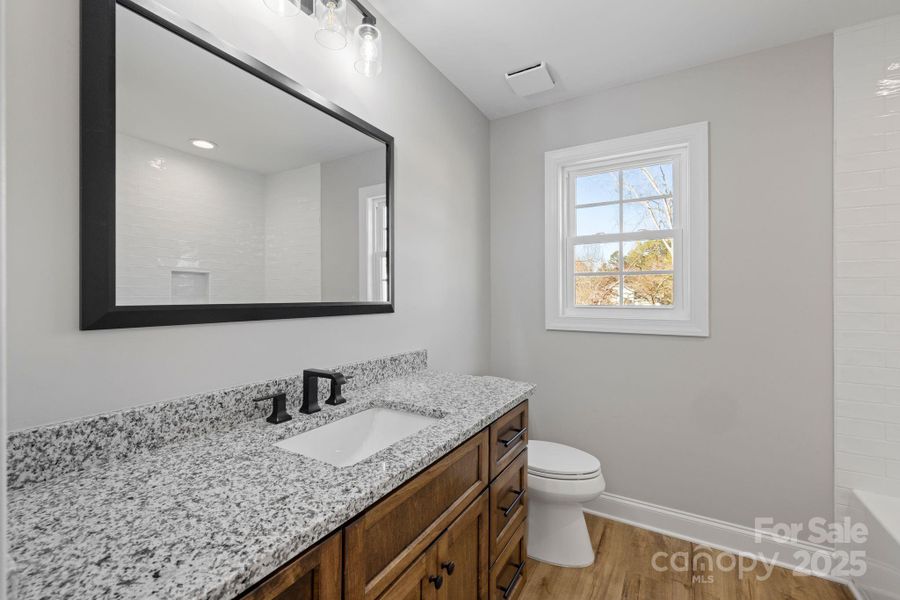Jack & Jill bathroom featuring custom wood cabinetry, granite countertop, modern black fixtures, and a large framed mirror. Jack & Jill bathroom featuring custom wood cabinetry, granite countertop, modern black fixtures, and a large framed mirror.
