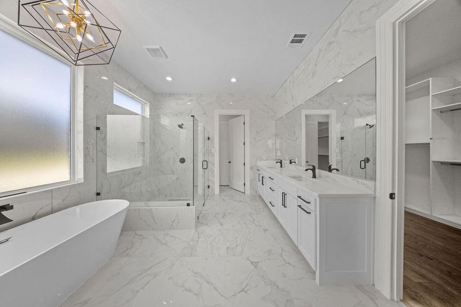 Full bath with double vanity, a marble finish shower, a freestanding bath, a spacious closet, and suspended lighting