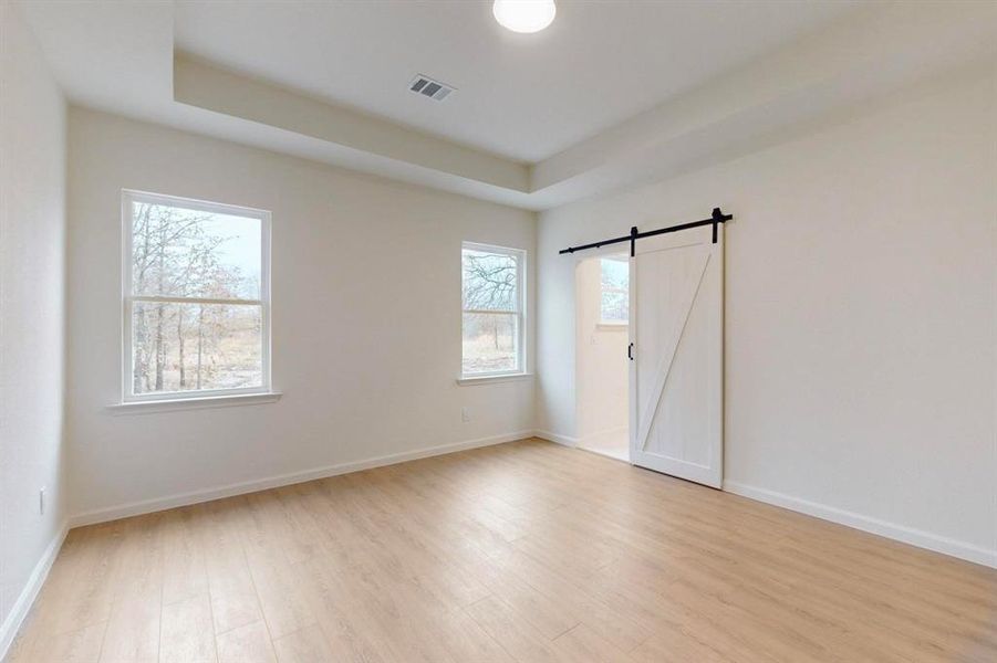 Unfurnished room featuring a barn door, light wood-style floors, visible vents, and baseboards