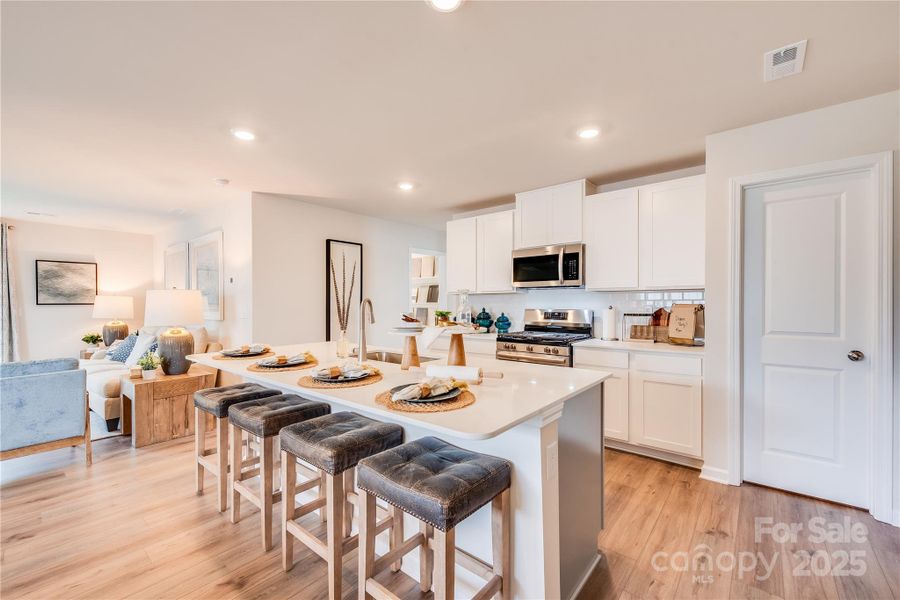 Spacious kitchen with white cabinets, a large island, stainless appliances and a gas range. The refrigerator is also included.