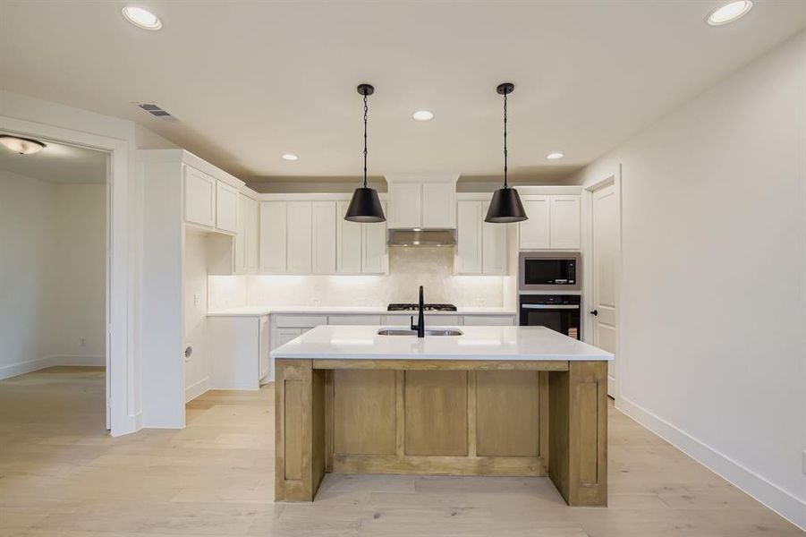 Kitchen with white cabinetry, recessed lighting, backsplash, and light wood-style floors Kitchen with white cabinetry, recessed lighting, backsplash, and light wood-style floors