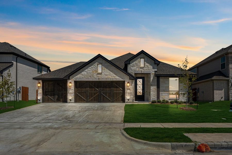 Single-story home with stone exterior, two-car garage with wood doors, and green front lawn at dusk.