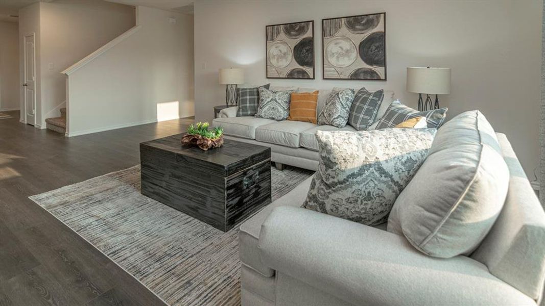 Open-concept living area featuring wood-finish flooring, light neutral wall paint, and a staircase with carpeted treads