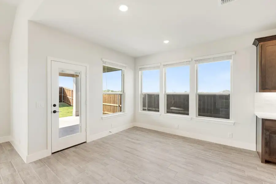 Bright dining area with light wood-look tile floors, three windows, and glass back door to patio