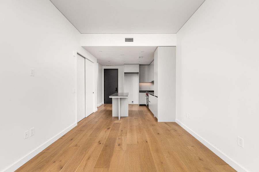 A well-lit, open-concept living space with sleek kitchen cabinetry and natural wood flooring.
