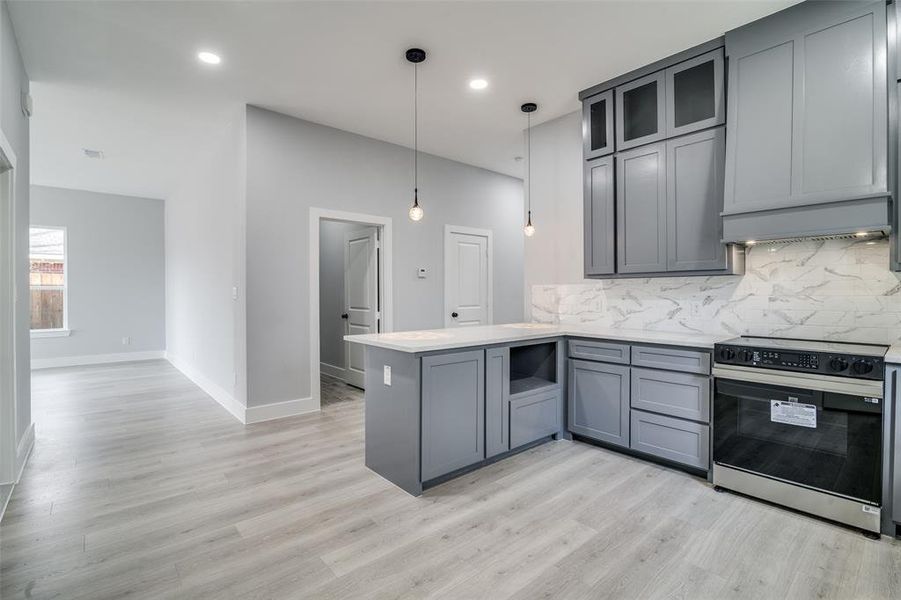 Kitchen with hanging light fixtures, light hardwood / wood-style flooring, decorative backsplash, stainless steel range oven, and kitchen peninsula