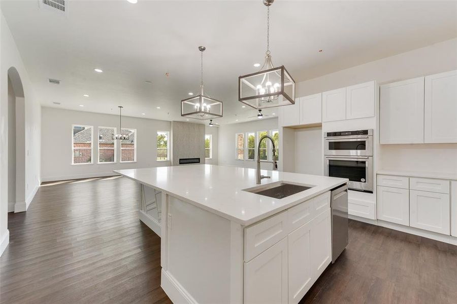 Kitchen with dark wood-type flooring, sink, hanging light fixtures, white cabinets, and an island with sink