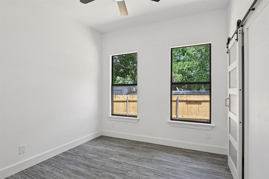 Spare room featuring a barn door, ceiling fan, and dark wood-style floors Spare room featuring a barn door, ceiling fan, and dark wood-style floors
