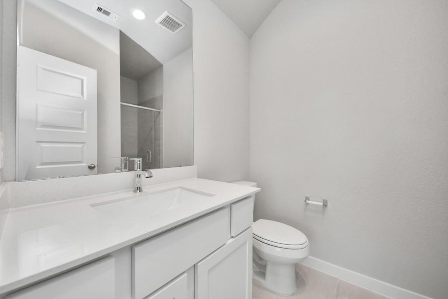 Secondary bath features tile flooring, a walk-in shower with tile surround, light stained wood cabinets, beautiful light countertop. Sample photo of completed home with similar floor plan. Actual colors and selections may vary.