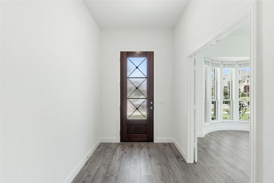 Entryway with dark wood front door featuring glass panels and gray hardwood floors leading to a bay window room Entryway with dark wood front door featuring glass panels and gray hardwood floors leading to a bay window room