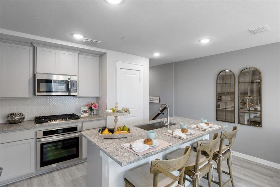 Kitchen featuring sink, light stone countertops, a breakfast bar, appliances with stainless steel finishes, and light hardwood / wood-style floors