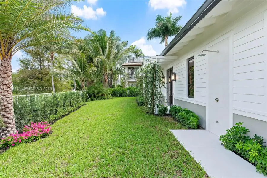 Exterior featuring horizontal lap siding, manicured lawn, established perimeter landscaping, palm trees, and a wall-mounted outdoor shower fixture Exterior featuring horizontal lap siding, manicured lawn, established perimeter landscaping, palm trees, and a wall-mounted outdoor shower fixture