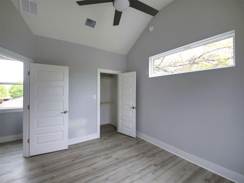 Unfurnished bedroom with a walk in closet, light wood finished floors, a ceiling fan, and high vaulted ceiling