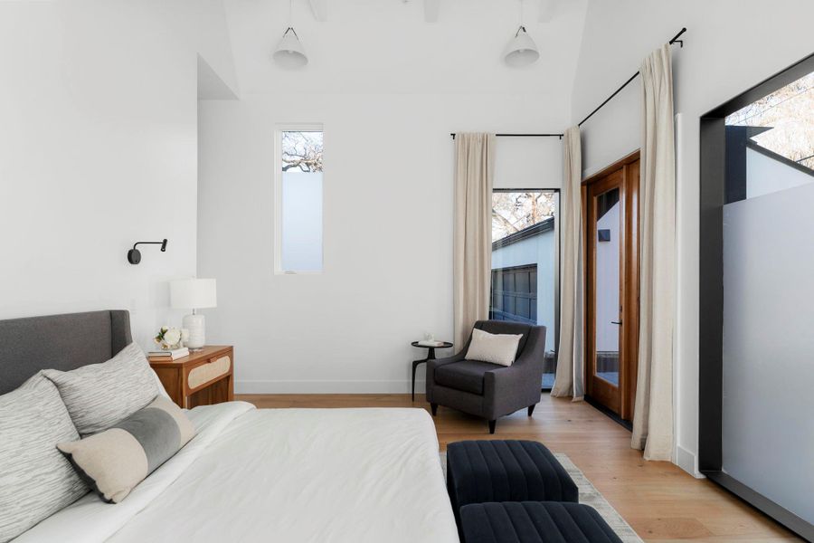 Bedroom featuring light wood-type flooring, multiple windows, and a high ceiling