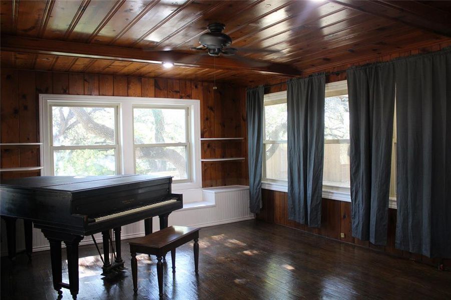 Sitting room featuring wooden walls, dark wood-type flooring, a wood ceiling with exposed beams, and a ceiling fan Sitting room featuring wooden walls, dark wood-type flooring, a wood ceiling with exposed beams, and a ceiling fan
