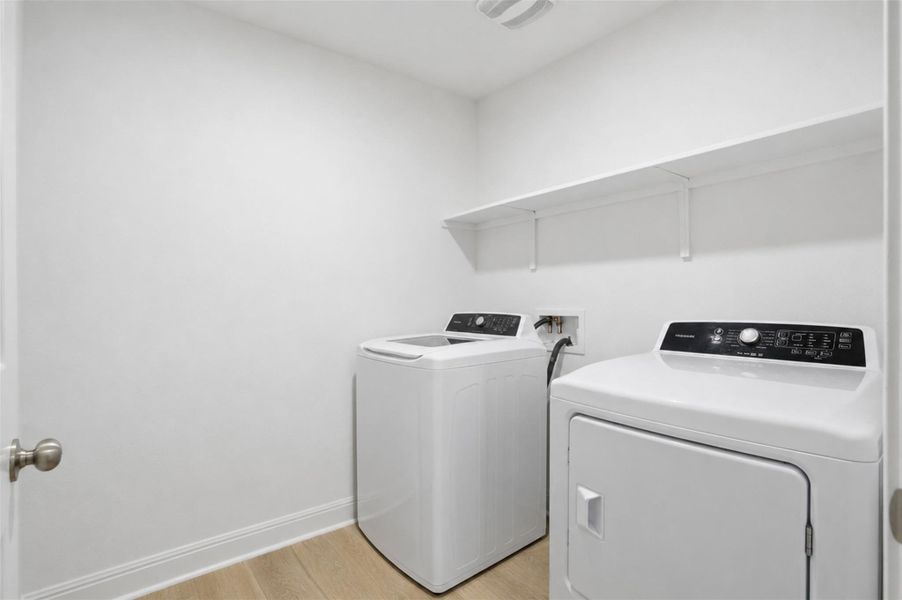 Dedicated laundry area featuring wood-finish flooring, white walls, and a full-width shelving unit