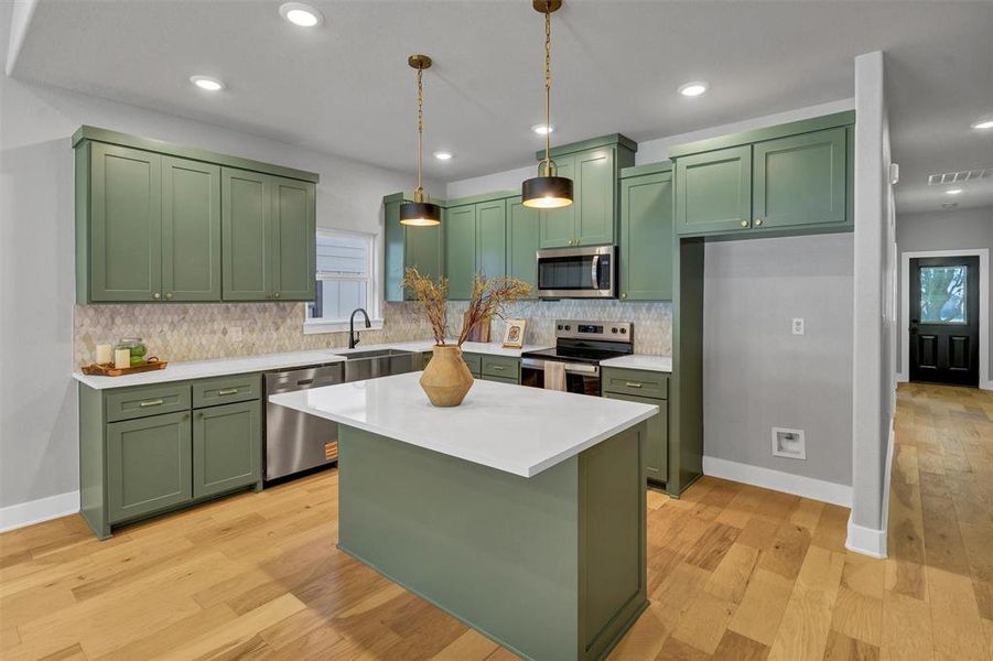 Kitchen featuring green cabinets, appliances with stainless steel finishes, a center island, light wood-style floors, and recessed lighting