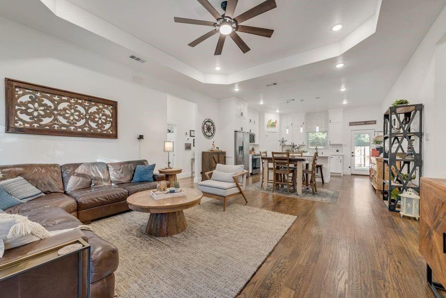 Living area featuring ceiling fan, dark wood-type flooring, a raised ceiling, and recessed lighting