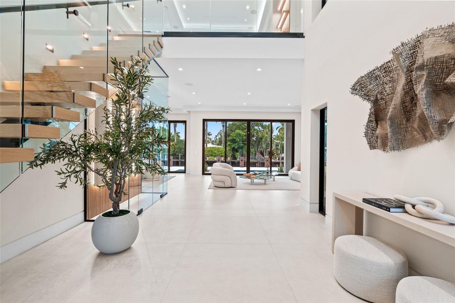 Dramatic two-story foyer with floating glass staircase, modern art accents, and direct views to the pool and waterfront beyond. Dramatic two-story foyer with floating glass staircase, modern art accents, and direct views to the pool and waterfront beyond.