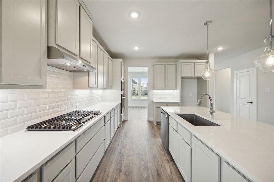 Kitchen with decorative backsplash, stainless steel appliances, sink, wood-type flooring, and hanging light fixtures