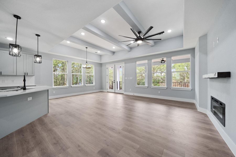Open-concept living area with wood-finish flooring, a tray ceiling featuring recessed lighting and exposed beams, and multiple windows