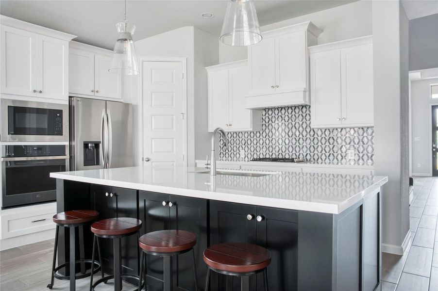 This modern kitchen features a large island with a sleek countertop and seating for four. It includes stainless steel appliances, white cabinetry, and a stylish geometric backsplash, offering a bright and contemporary feel. This modern kitchen features a large island with a sleek countertop and seating for four. It includes stainless steel appliances, white cabinetry, and a stylish geometric backsplash, offering a bright and contemporary feel.