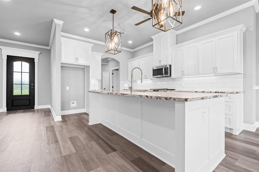 Kitchen with stainless steel microwave, white cabinetry, arched walkways, and a kitchen island with sink Kitchen with stainless steel microwave, white cabinetry, arched walkways, and a kitchen island with sink