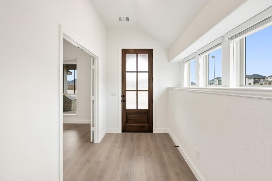 Entryway hallway with dark wood glass-panel door, white walls, and light hardwood floors Entryway hallway with dark wood glass-panel door, white walls, and light hardwood floors