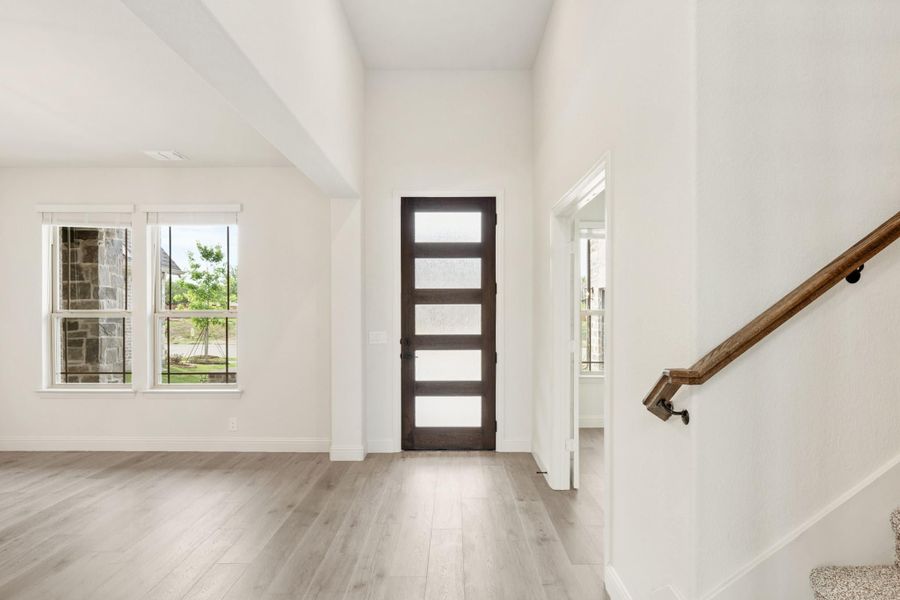 Bright entryway with dark wood glass-panel front door, light hardwood floors, and staircase with wood handrail Bright entryway with dark wood glass-panel front door, light hardwood floors, and staircase with wood handrail