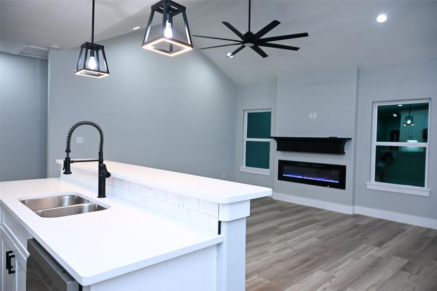 Kitchen featuring a glass covered fireplace, a center island with sink, pendant lighting, lofted ceiling, and dishwasher