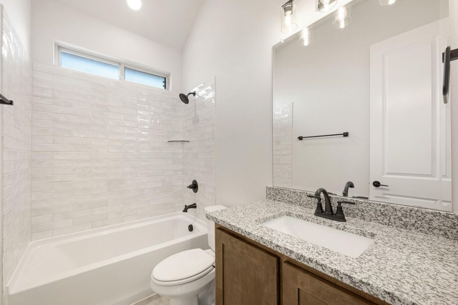 Bathroom with granite vanity, wood cabinets, white subway tile tub surround, and black fixtures Bathroom with granite vanity, wood cabinets, white subway tile tub surround, and black fixtures