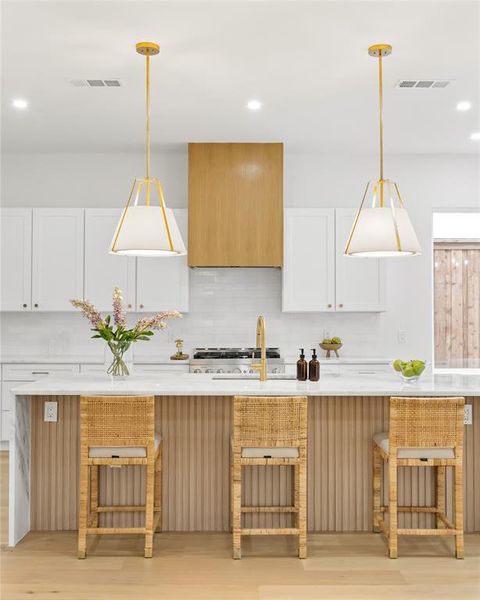 Kitchen featuring tasteful backsplash, hanging light fixtures, white cabinets, and a kitchen breakfast bar