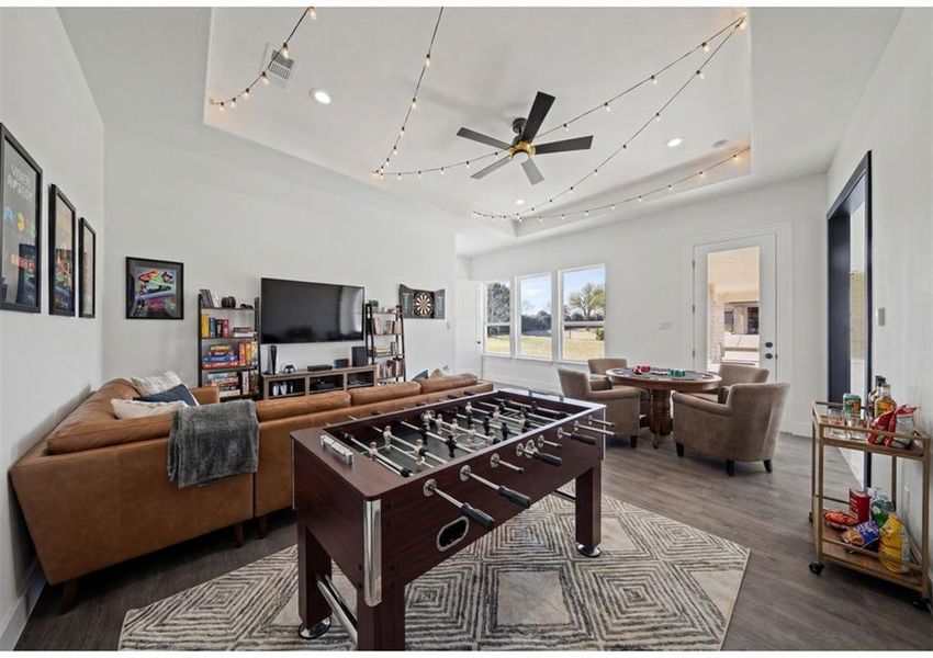 Virtually Staged - Recreation room with dark wood-style flooring, ceiling fan, a tray ceiling, and track lighting